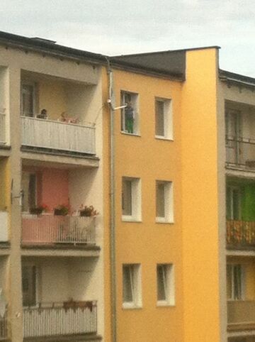 Pięciolatek stoi na parapecie okna, a mamuśka baluje na balkonie